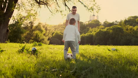 Father-and-child-play-football-standing-on-the-field-at-sunset.-The-boy-strikes-the-goal.-The-father-of-the-goalkeeper-is-on-the-gate-the-child-strikes-the-ball.